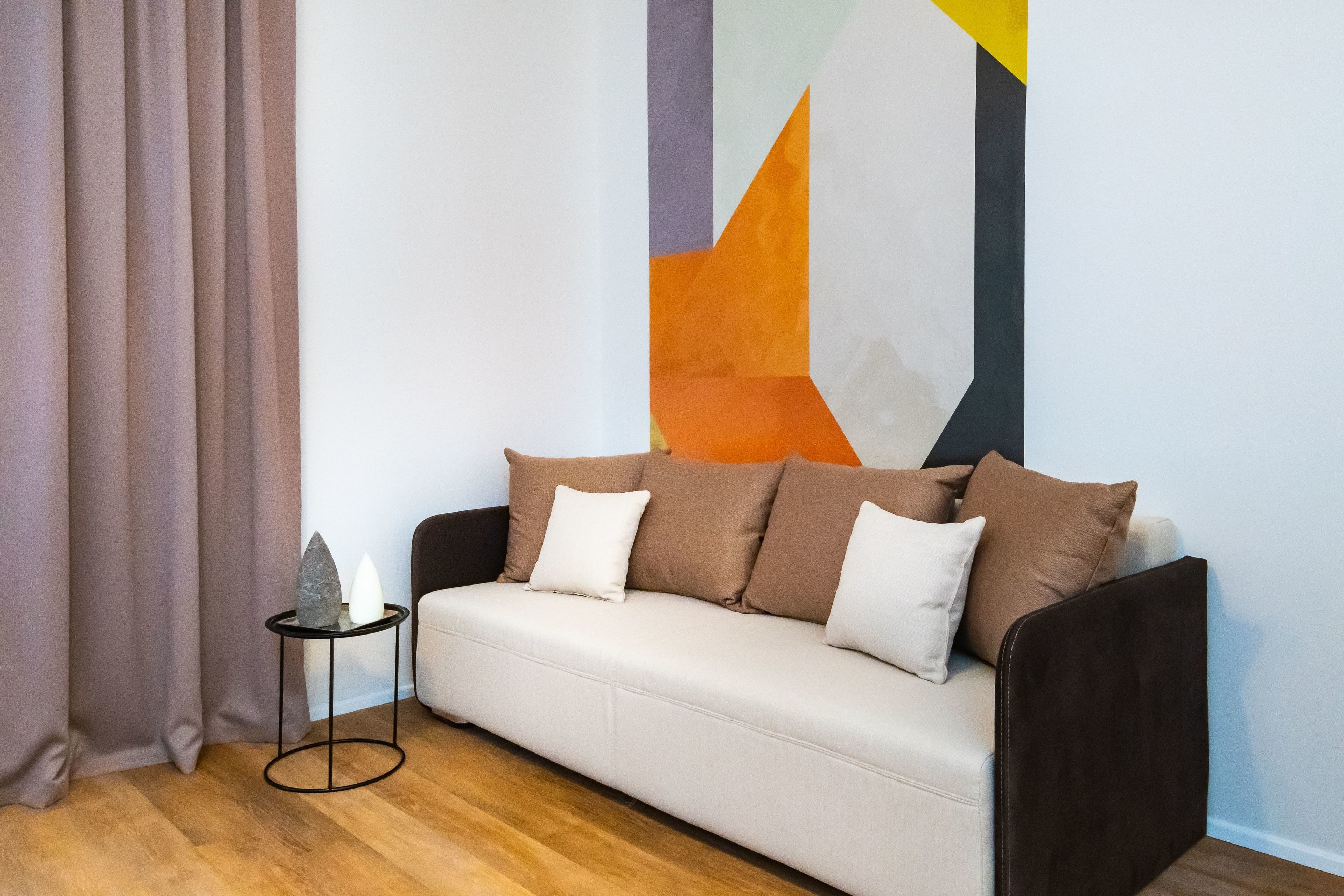A modern living room with a beige sofa, a small side table, and a geometric wall art piece.