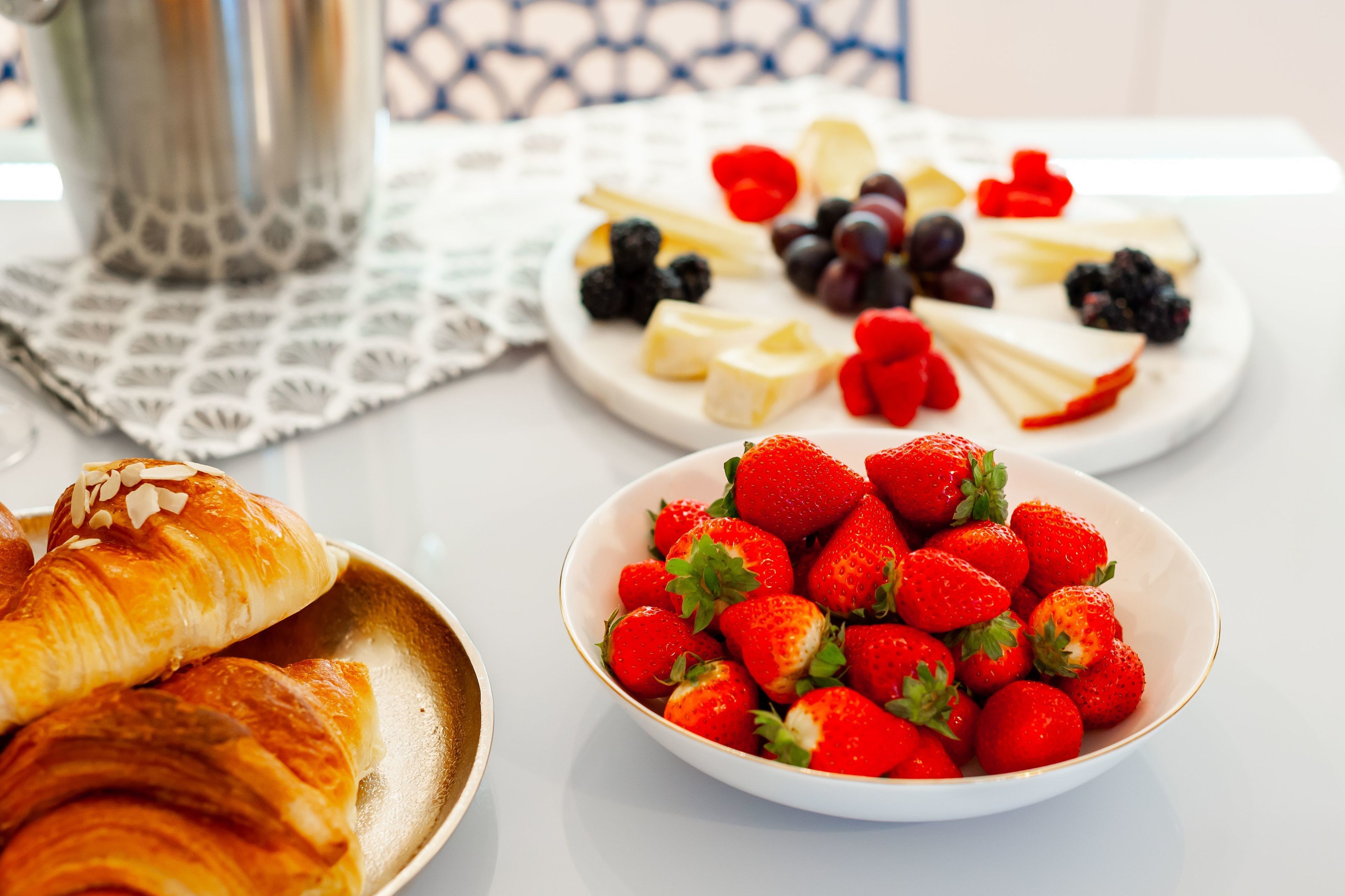 Ein Frühstückstisch mit Croissants, Erdbeeren und einer Käse- und Obstplatte.