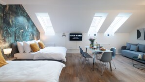 Een moderne, goed verlichte kamer met een groot bed, een eettafel met stoelen en een bank. Er zijn dakramen in het plafond en een bord aan de muur.