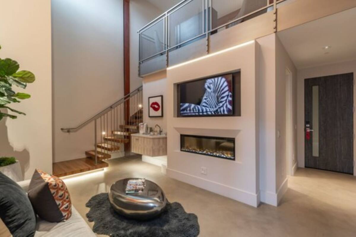 A modern living room with a fireplace, a staircase, and a flat-screen TV mounted on the wall.