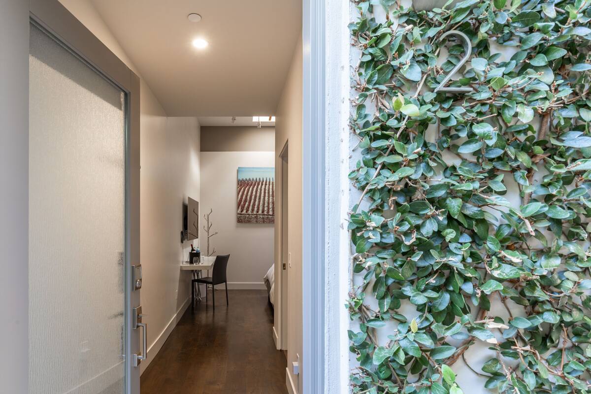 A hallway with a glass door, a dining area with chairs and a table, and a wall covered in green foliage.