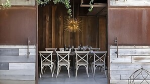 An outdoor dining area with a rustic wooden backdrop, a decorative light fixture, and white wicker chairs.