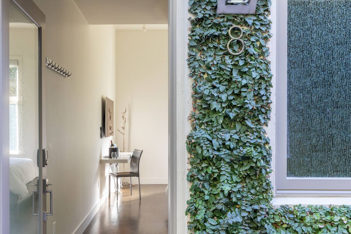 A hallway with a glass door, a dining area with a table and chairs, and a wall covered with green foliage.