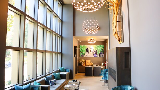 A modern interior with large windows, a seating area with blue chairs, and a unique light fixture.