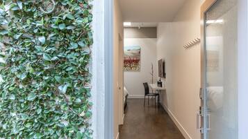 A hallway with a wall covered in green foliage, a desk with a chair, and a bed in the background.