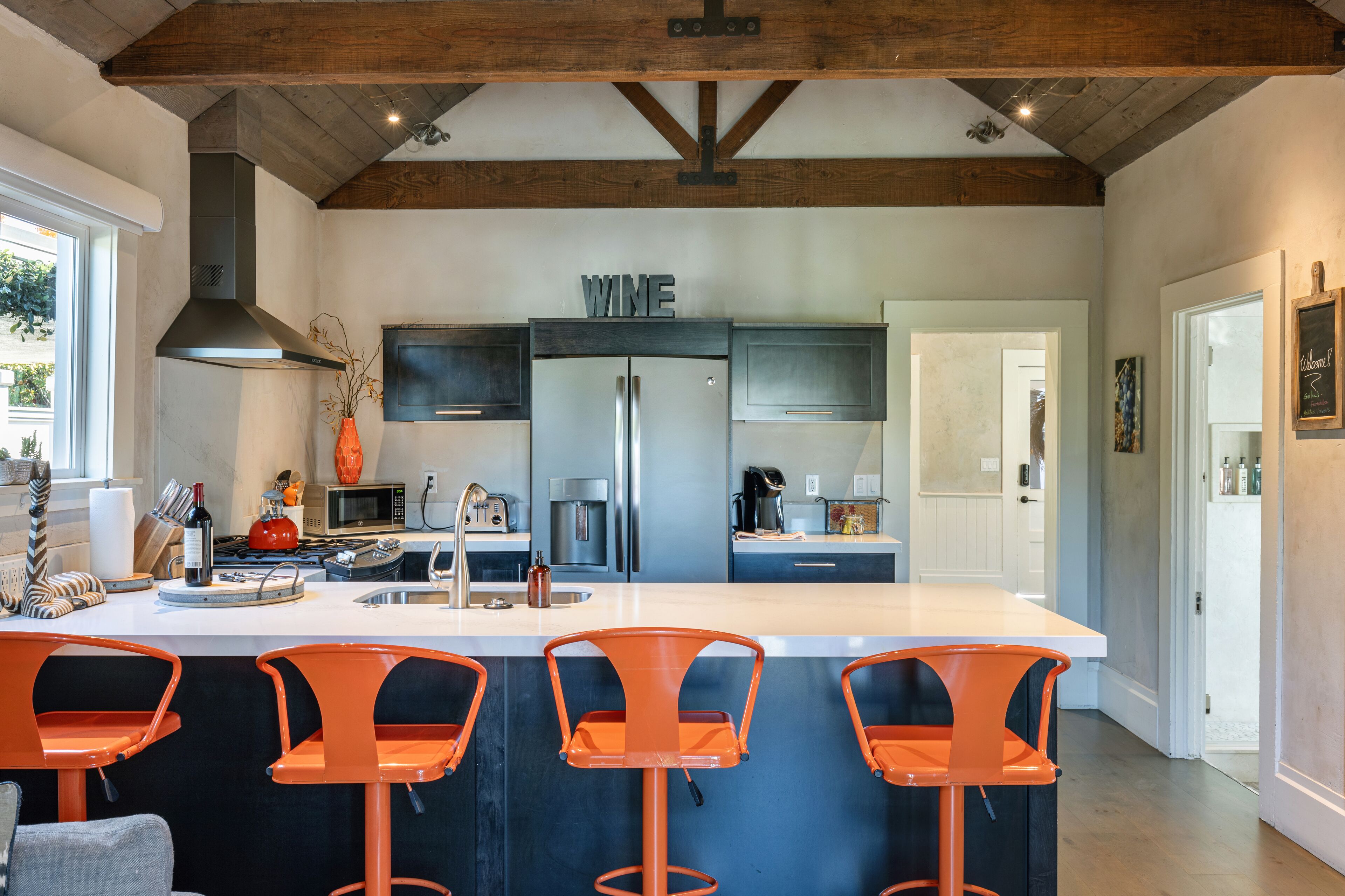 Une cuisine moderne dotée d’un îlot central, d’appareils électroménagers en acier inoxydable et de tabourets de bar orange.