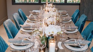 A long dining table set for a formal meal with blue upholstered chairs, candles, and white flowers.