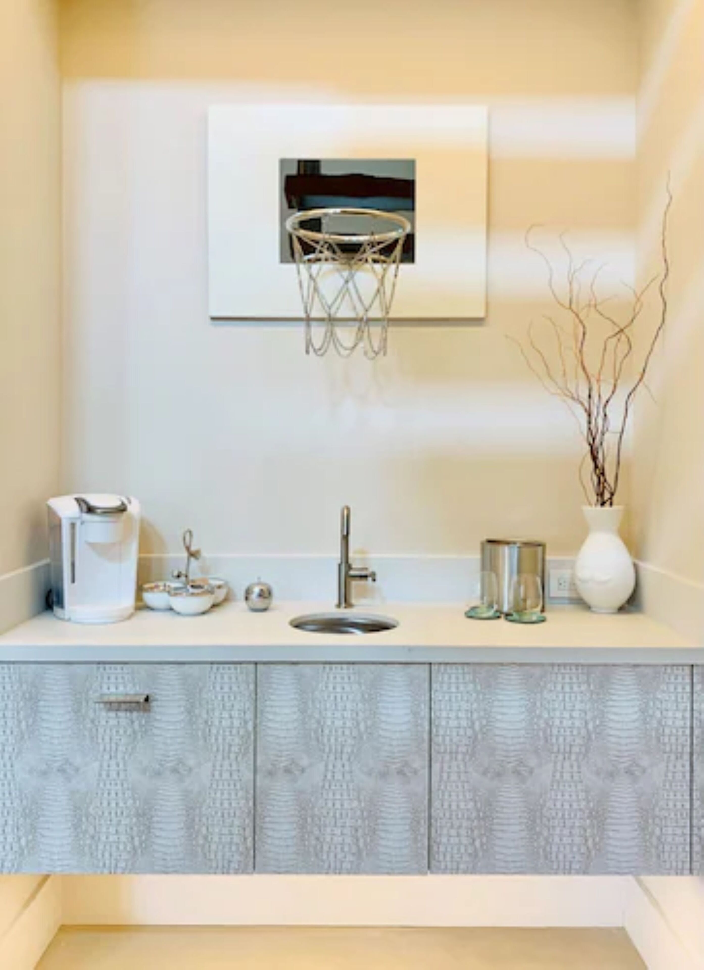A modern bathroom with a sink, a coffee maker, and a vase with branches.