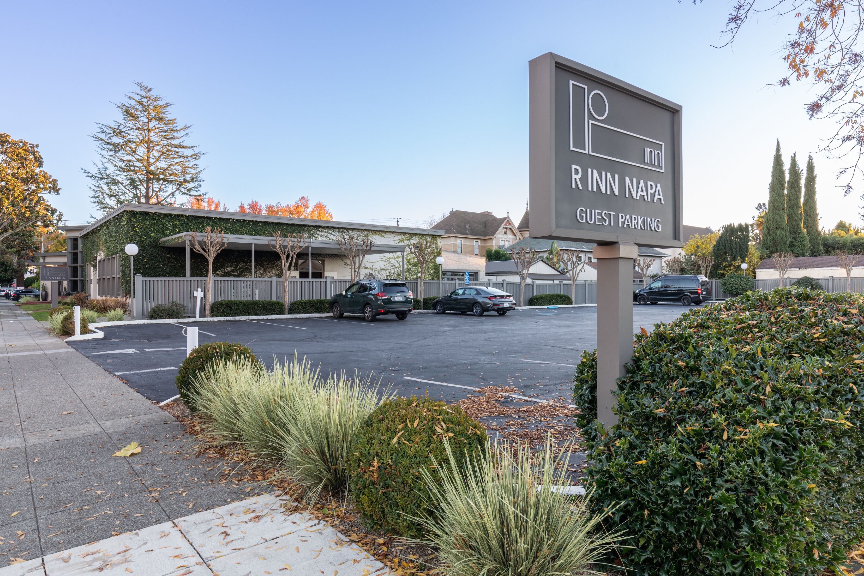 A sign for Rinn Inn Napa Guest Parking with a parking lot and buildings in the background.