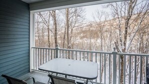 A covered outdoor area with a table and chairs, a white railing, and a view of leafless trees and a hilly landscape. - Cozy condo - Walk to village/mountain - Monthly rates (Mont-Tremblant)