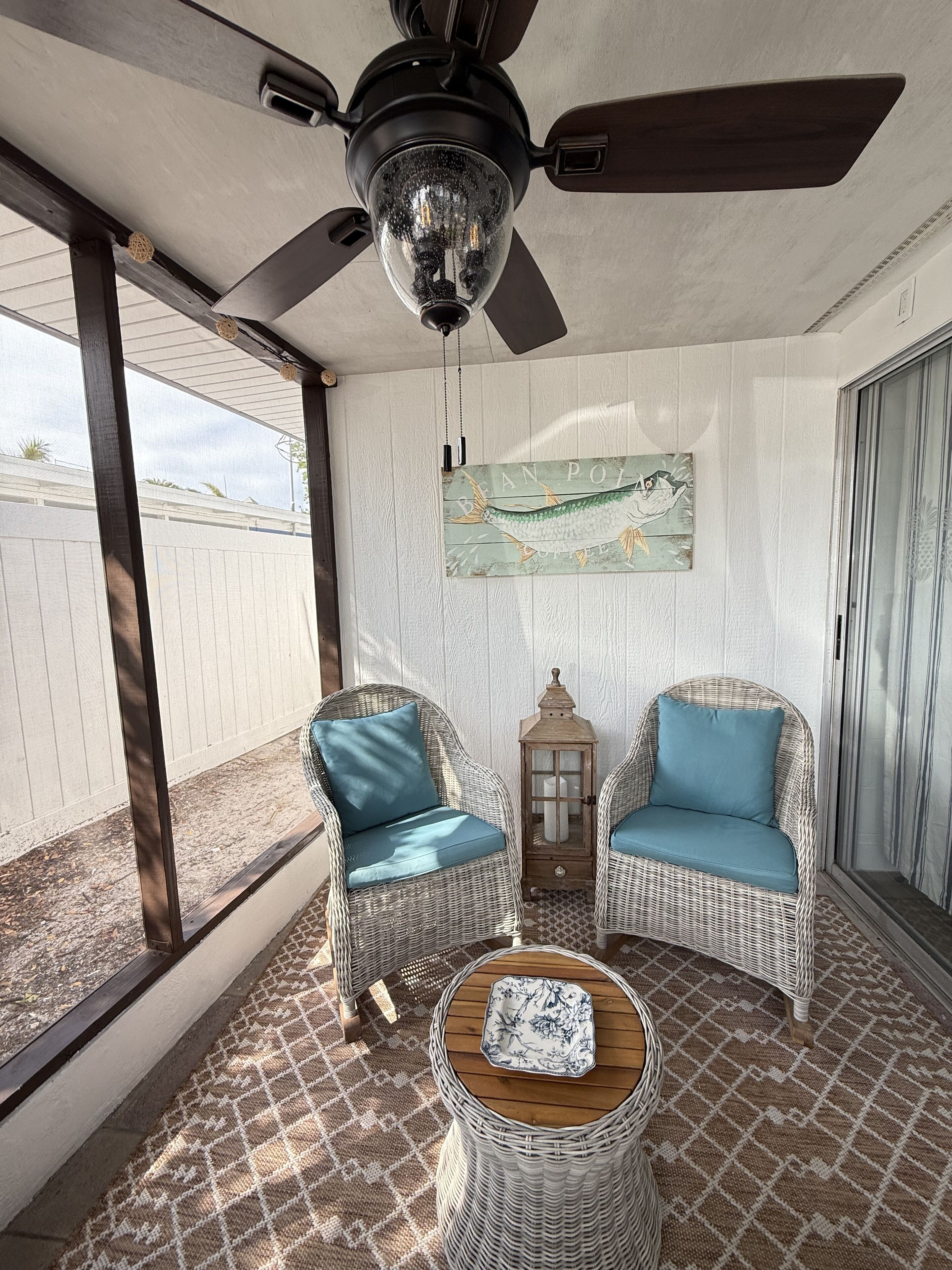 A sunlit room with wicker furniture, a ceiling fan, and a decorative lantern.