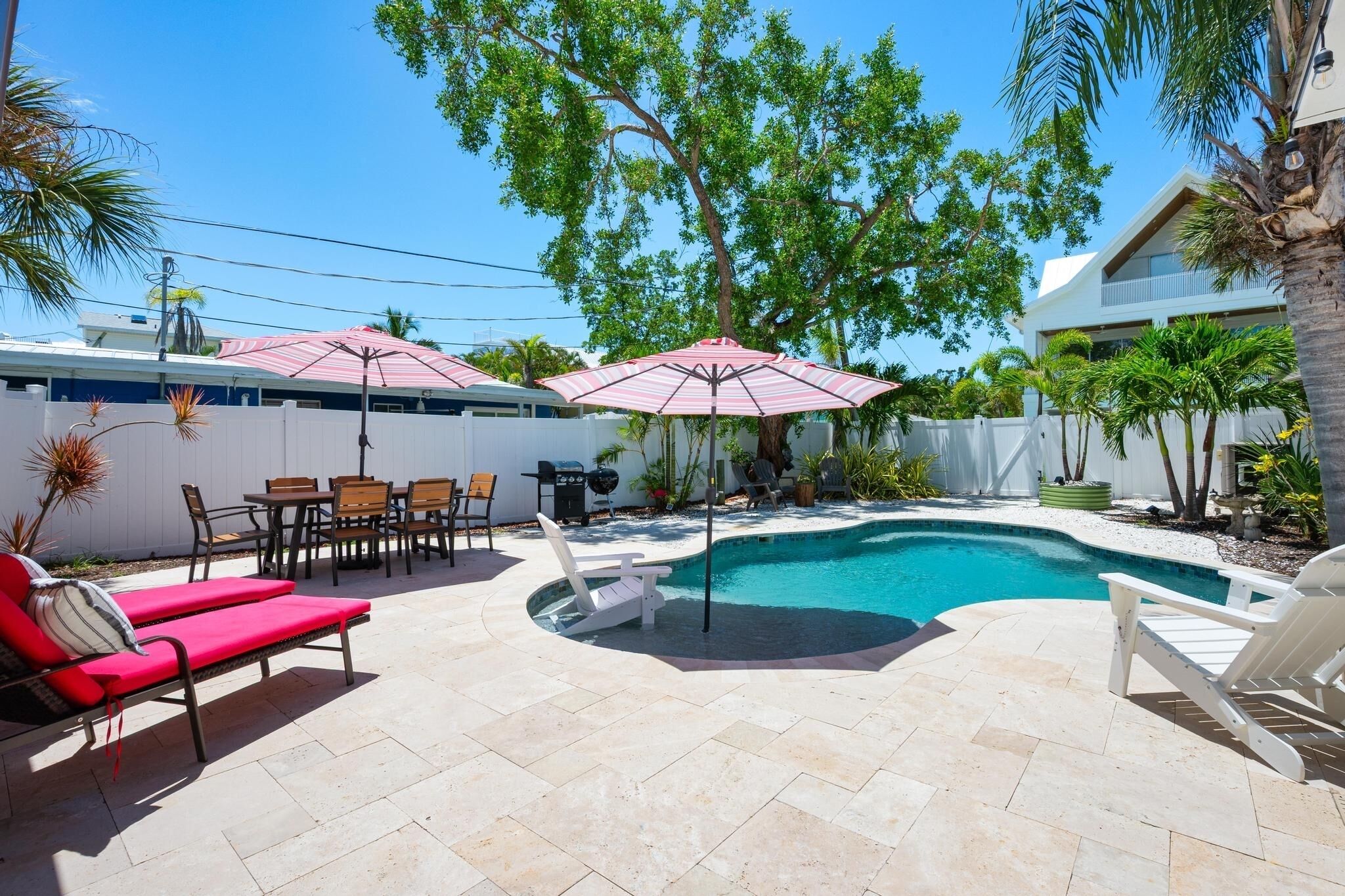 Un jardin avec une piscine, des chaises longues et un coin repas agrémenté de parasols.
