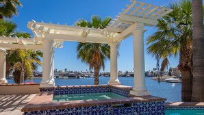 A pool area with a pergola, palm trees, and a view of the water.