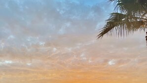 A balcony with a view of a sunset over a body of water, a large pot, and a chair.
