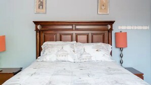 Een opgemaakt bed met een houten hoofdeinde, twee nachtkastjes en een wandlamp.