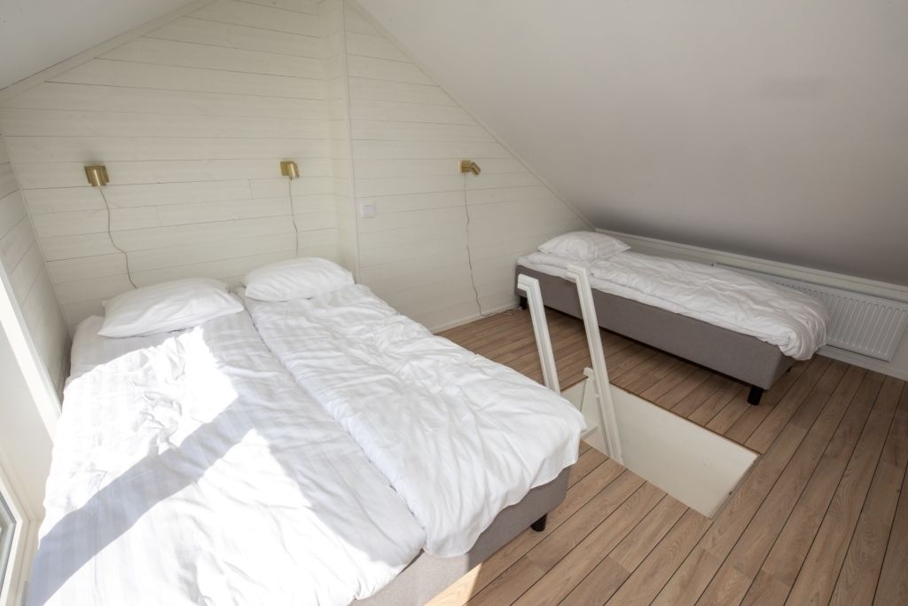 Una habitación pequeña con dos camas, techo inclinado y suelo de madera.