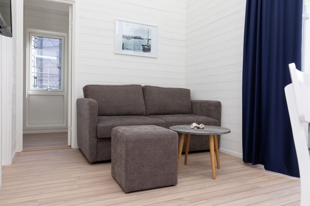 A room with a grey sofa, a small ottoman, a round table, and a framed picture on the wall.