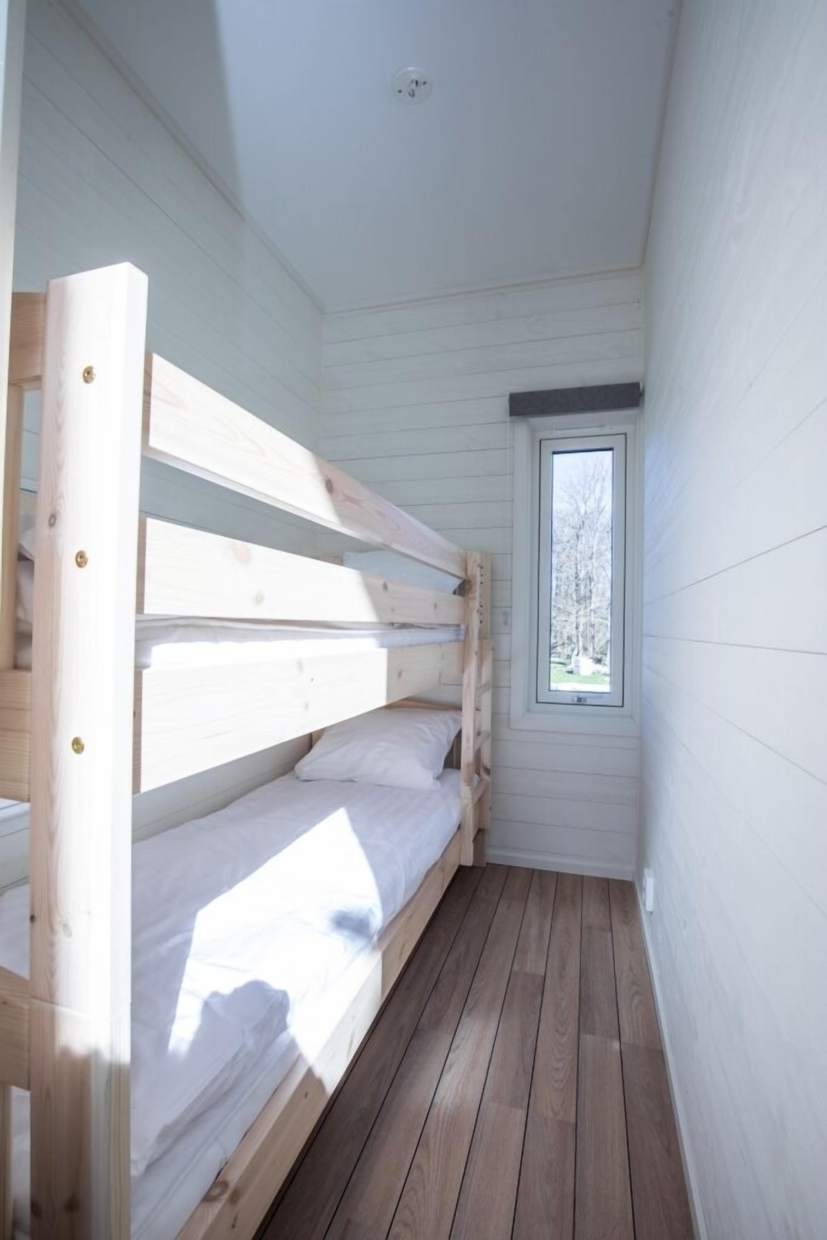 A narrow room with a bunk bed, a small window, and wooden flooring.