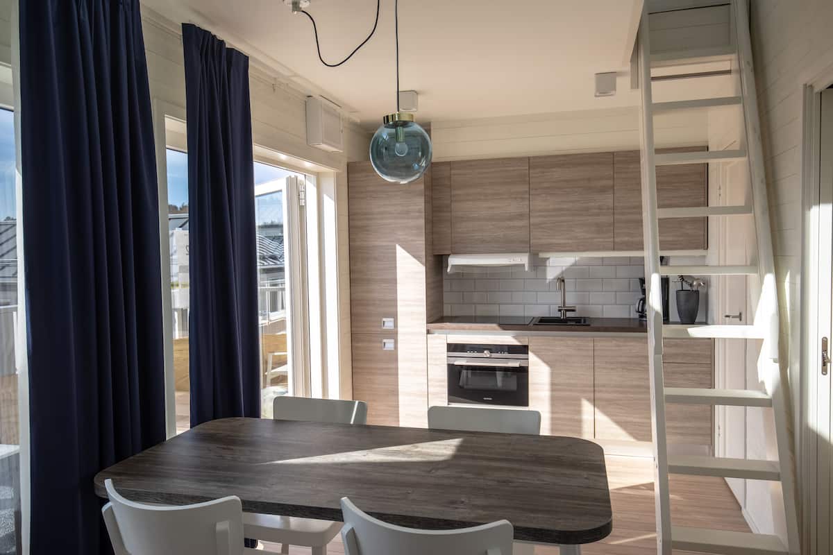 A modern kitchen with wooden cabinets, a built-in oven, and a dining area with a wooden table and white chairs.