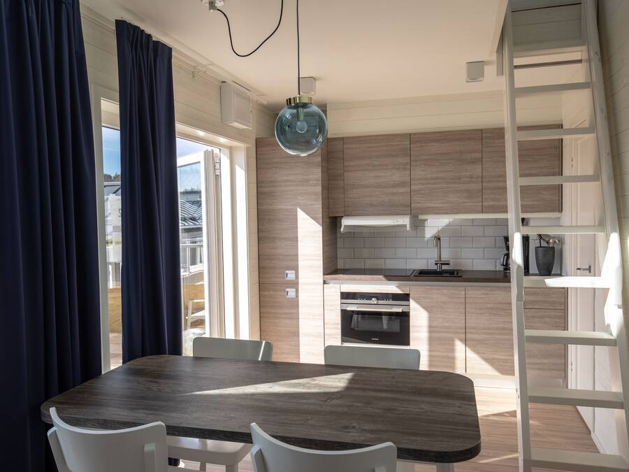 A modern kitchen with wooden cabinets, a built-in oven, and a dining area with a wooden table and white chairs.