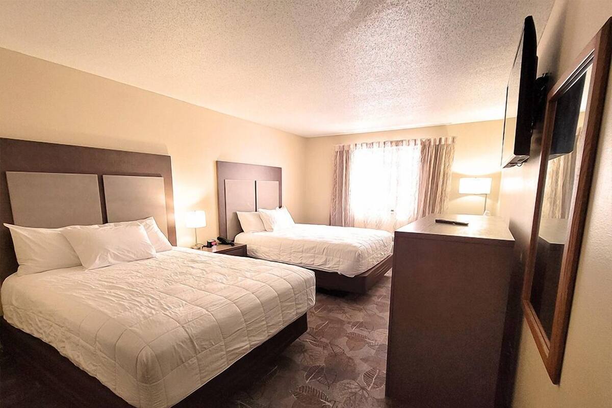 A hotel room with two beds, a desk, a TV, and a window with curtains.