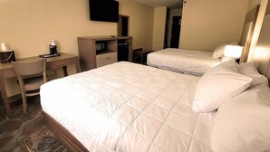 Habitación de hotel con dos camas, un escritorio, una silla, un televisor y una cafetera.
