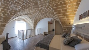 A bedroom with a vaulted stone ceiling, a bed with pillows, and a view of a balcony. - Clara Domus (Gallipoli)