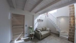 A spacious living area with a wooden door, a beige sofa, a staircase, and a stone wall. - Clara Domus (Gallipoli)