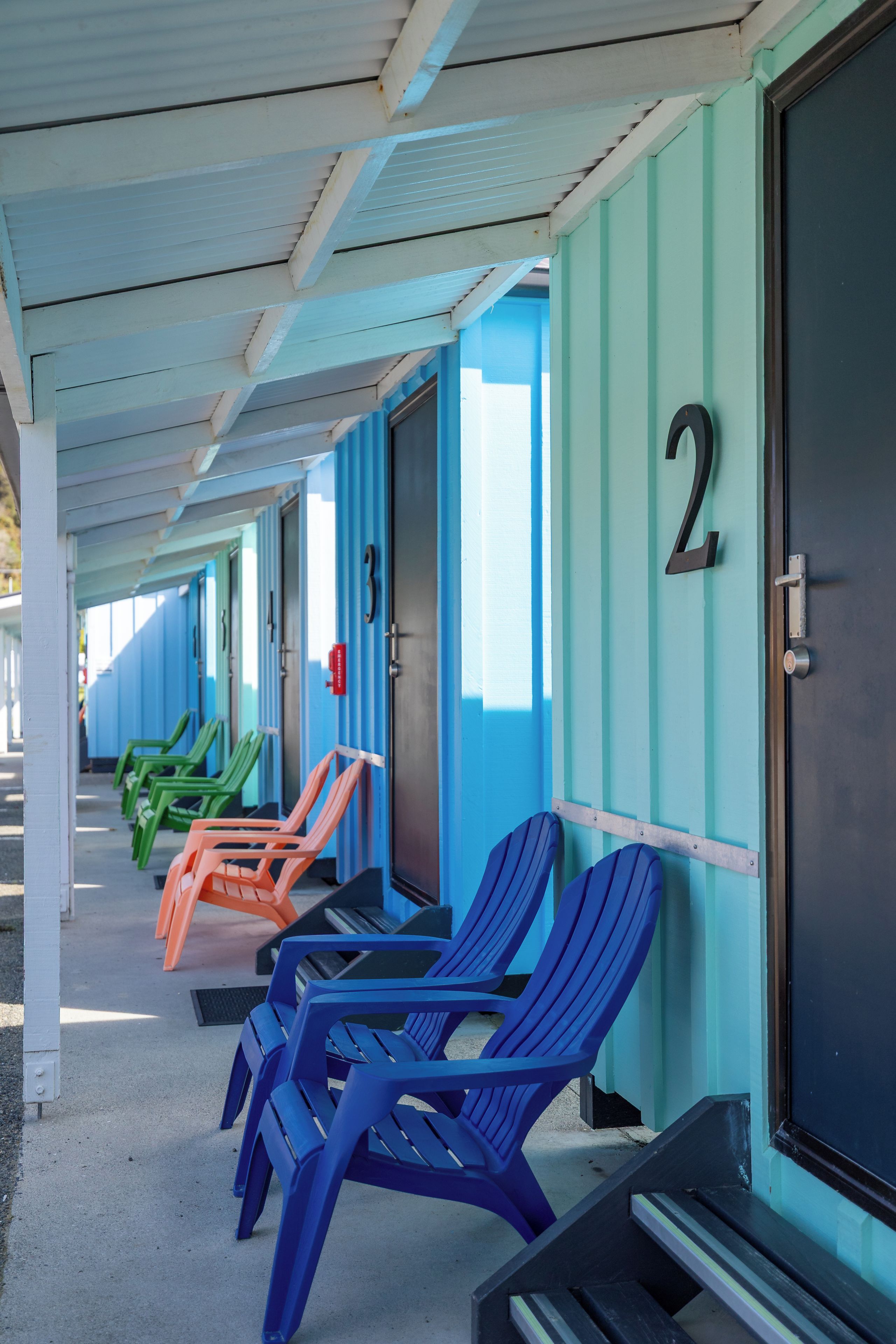 A row of motel rooms with numbered doors and plastic chairs outside.