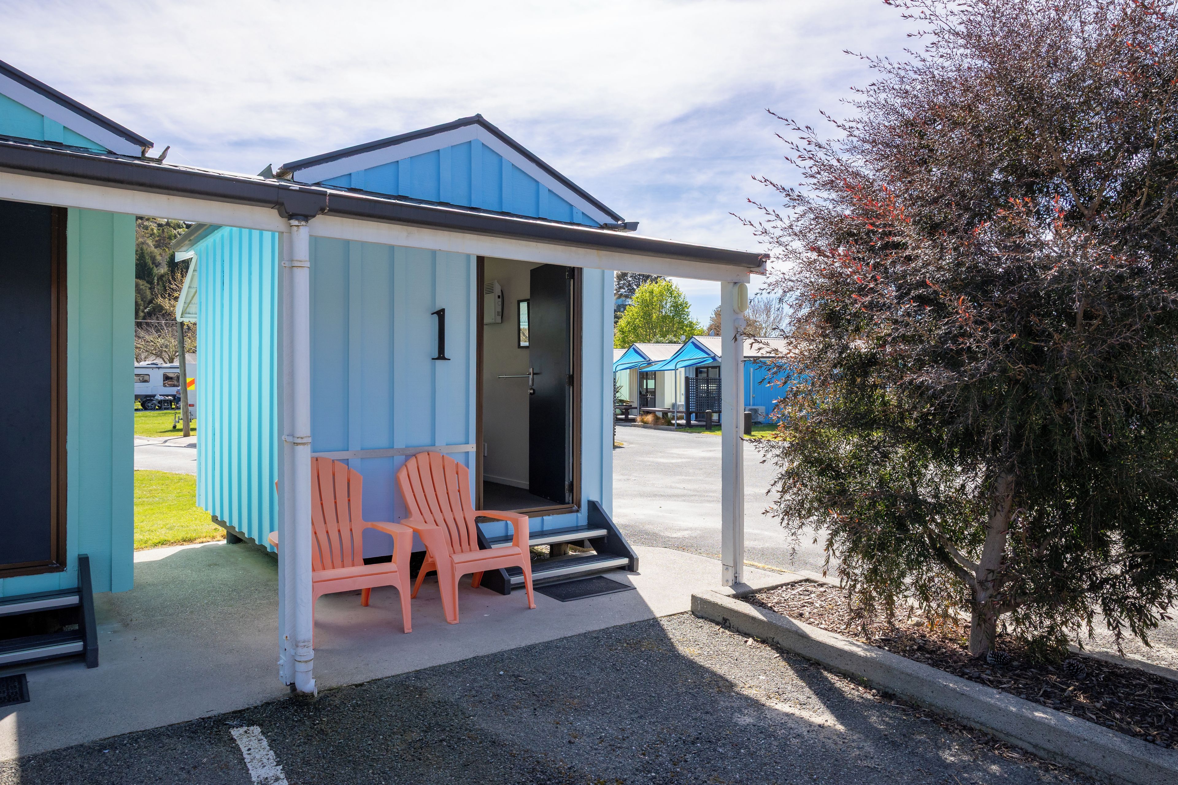 Un bâtiment à la façade bleue, avec la chambre numéro 1 et deux chaises à l’extérieur.