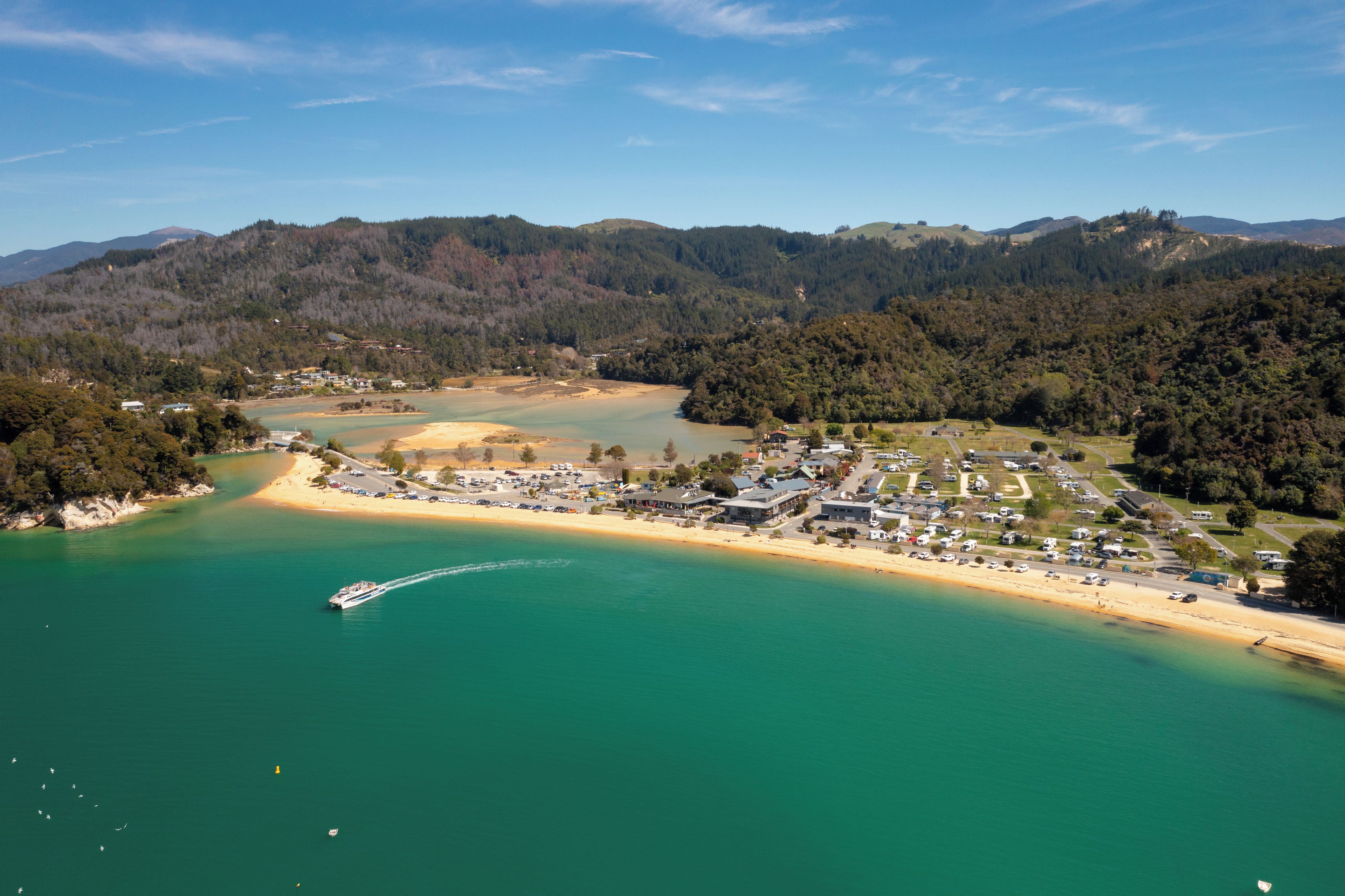 Vue aérienne d’une ville côtière avec une plage, des eaux cristallines et un bateau.