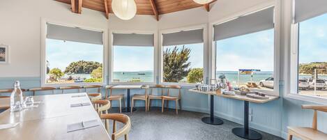 A dining area with wooden tables and chairs, large windows with ocean views, and hanging paper lanterns.