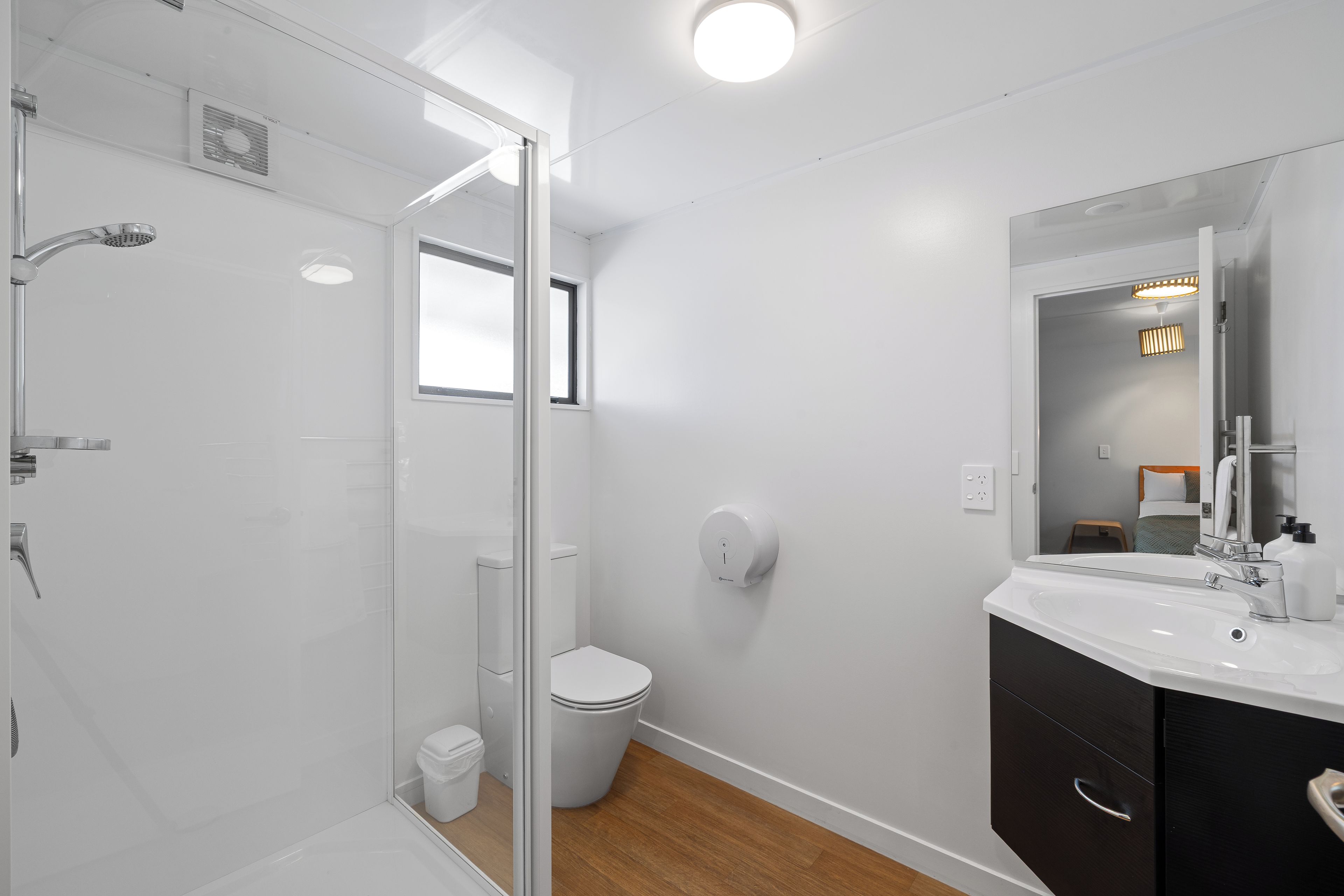 Une salle de bain moderne avec une douche à parois de verre, des toilettes, un lavabo avec un miroir et un plancher en bois.