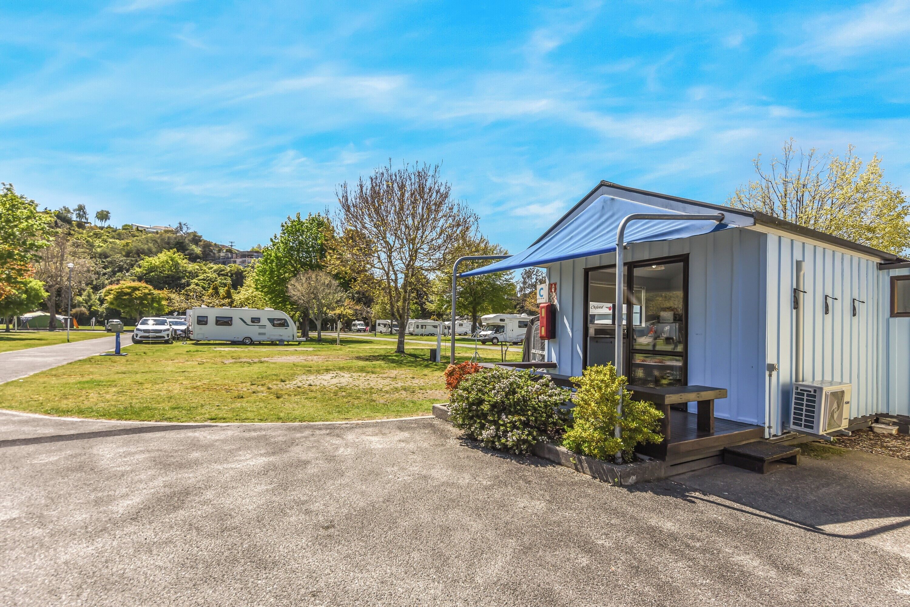 A small, single-story RV park with a covered outdoor area, a gravel driveway, and RVs parked in the background.