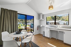 A modern kitchen with a dining area, large windows, and a view of the outdoors. - Kaiteriteri Reserve Cabins (Kaiteriteri)