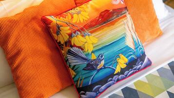 Una cama con un almohadón de colores que muestra un diseño floral y de pájaros, y una manta naranja con textura.