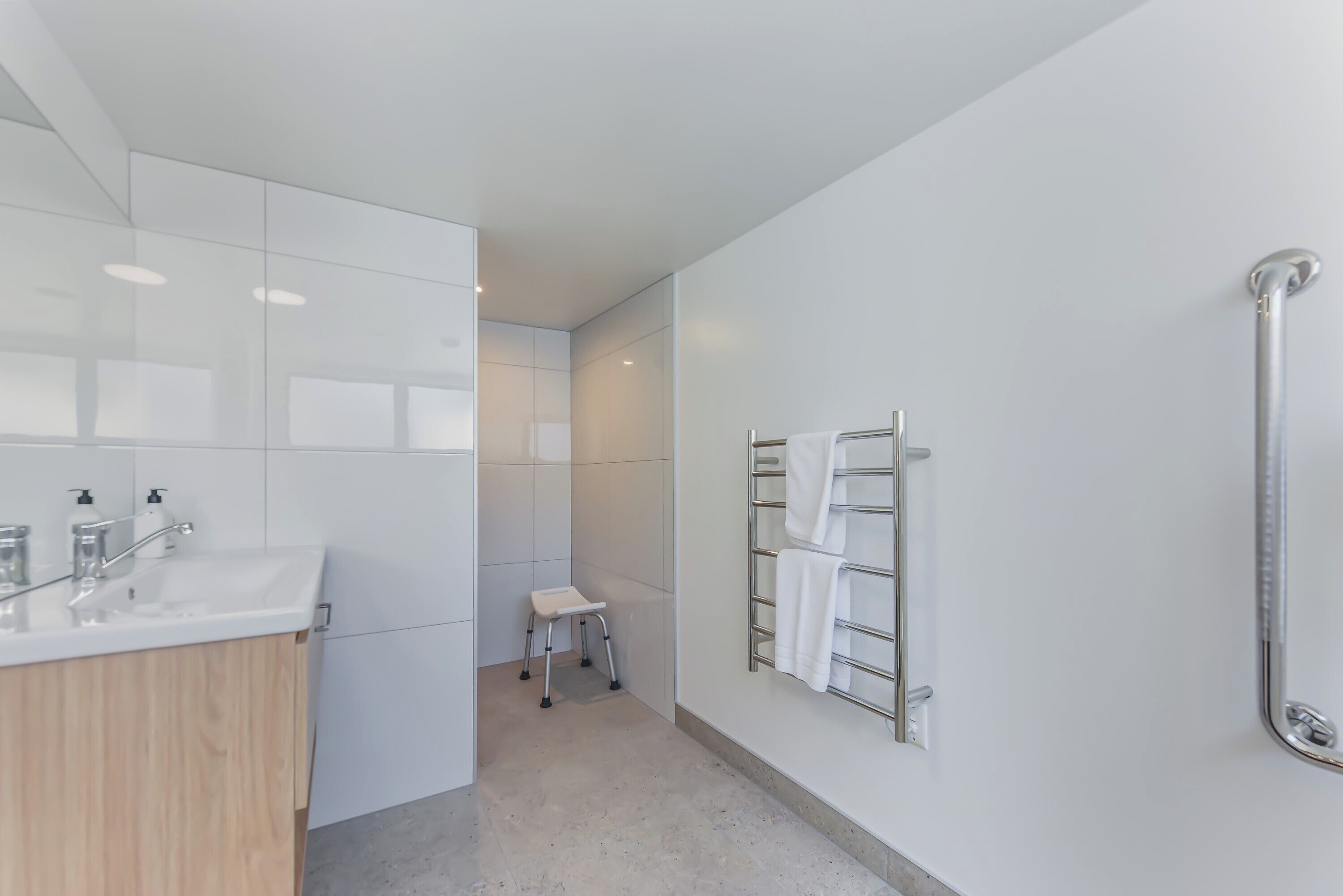 A modern bathroom with a white sink, a small stool, and a towel rack.
