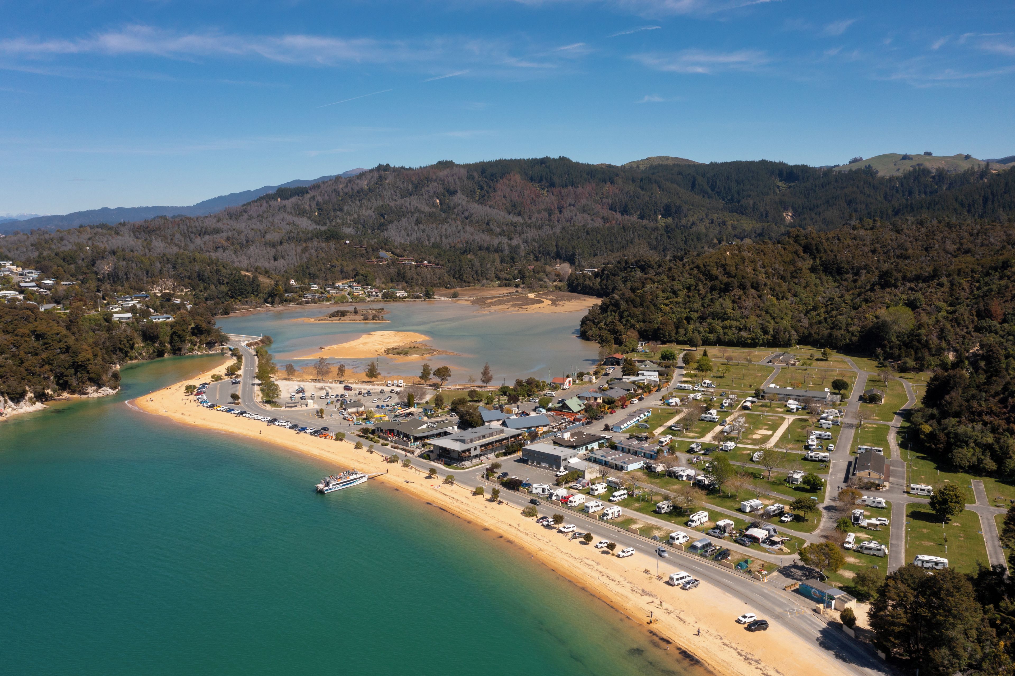 An aerial view of a coastal area with a beach, a marina, and a residential zone with RVs.