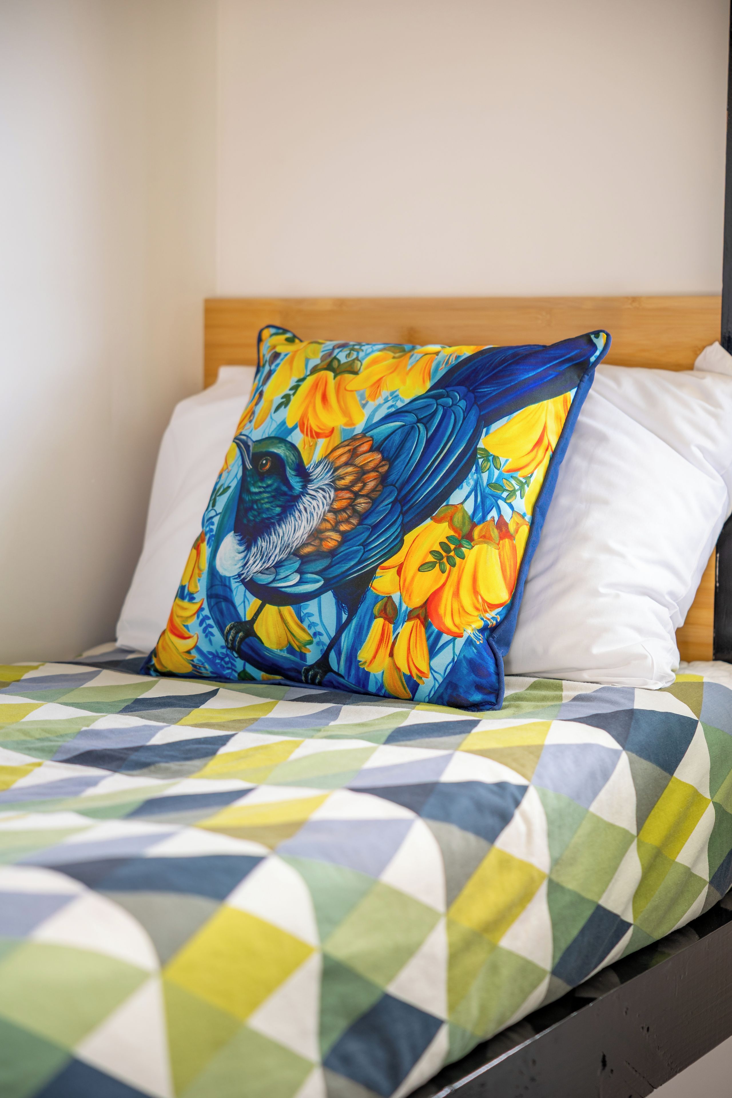 A bed with a colorful geometric-patterned bedspread and a pillow with a bird and floral design.