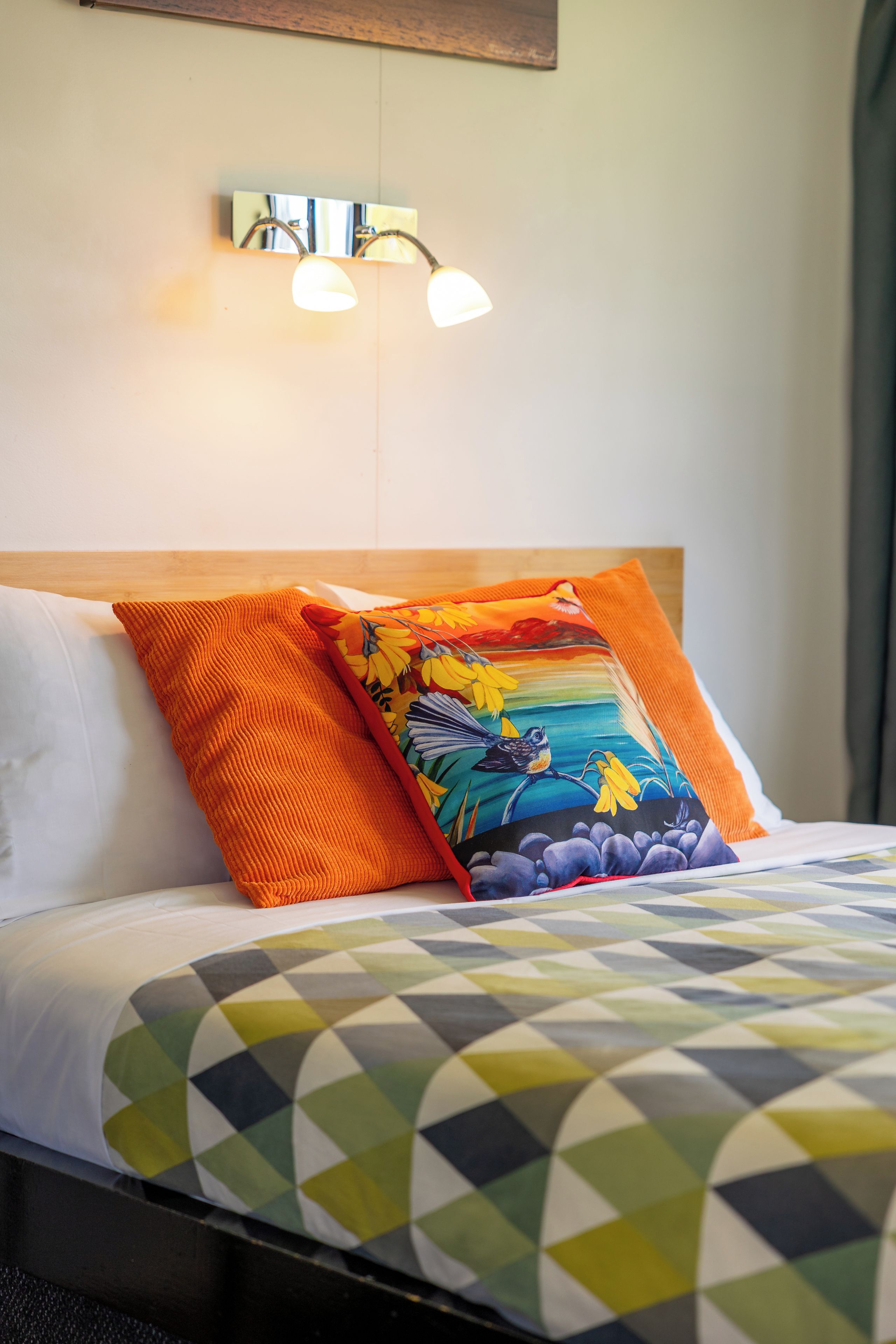Une chambre d’hôtel avec un lit, deux oreillers, un luminaire fixé au mur et une couvre-lit à motifs.