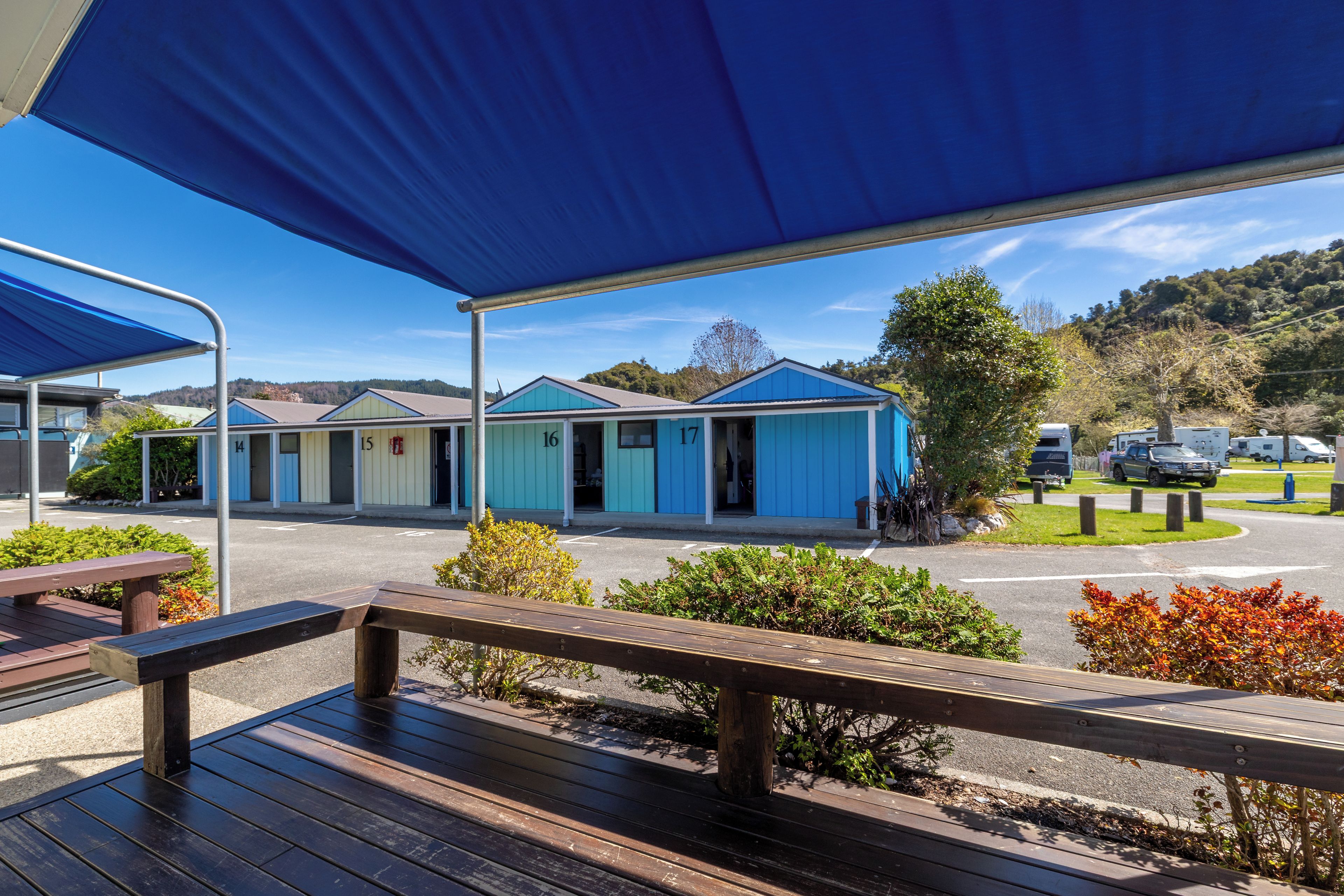 A row of blue mobile homes with numbered doors, a picnic table, and a parking area with RVs.
