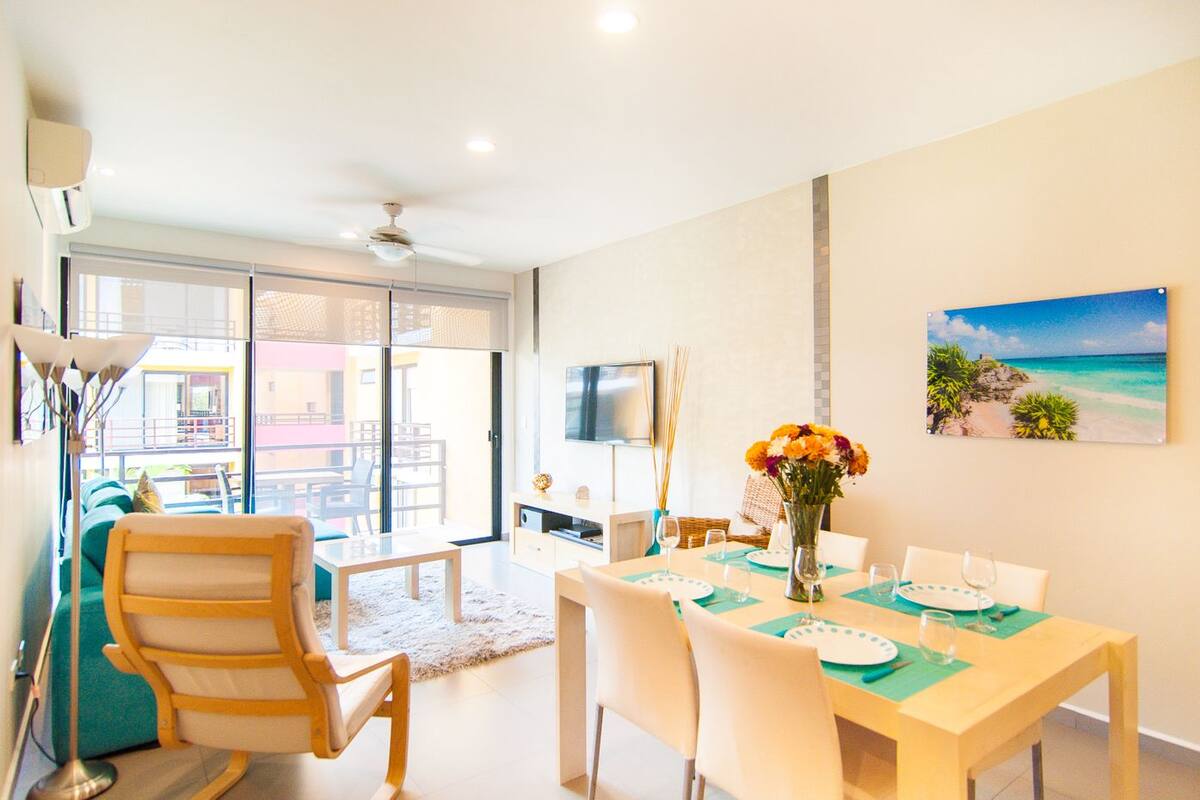 A modern dining area with a table set for four, a large window with a view of the outside, and a ceiling fan.