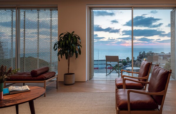 A modern living room with a large sliding glass door leading to a balcony with a city view. - The Jaffa – Fattal Limited Edition (Tel Aviv)