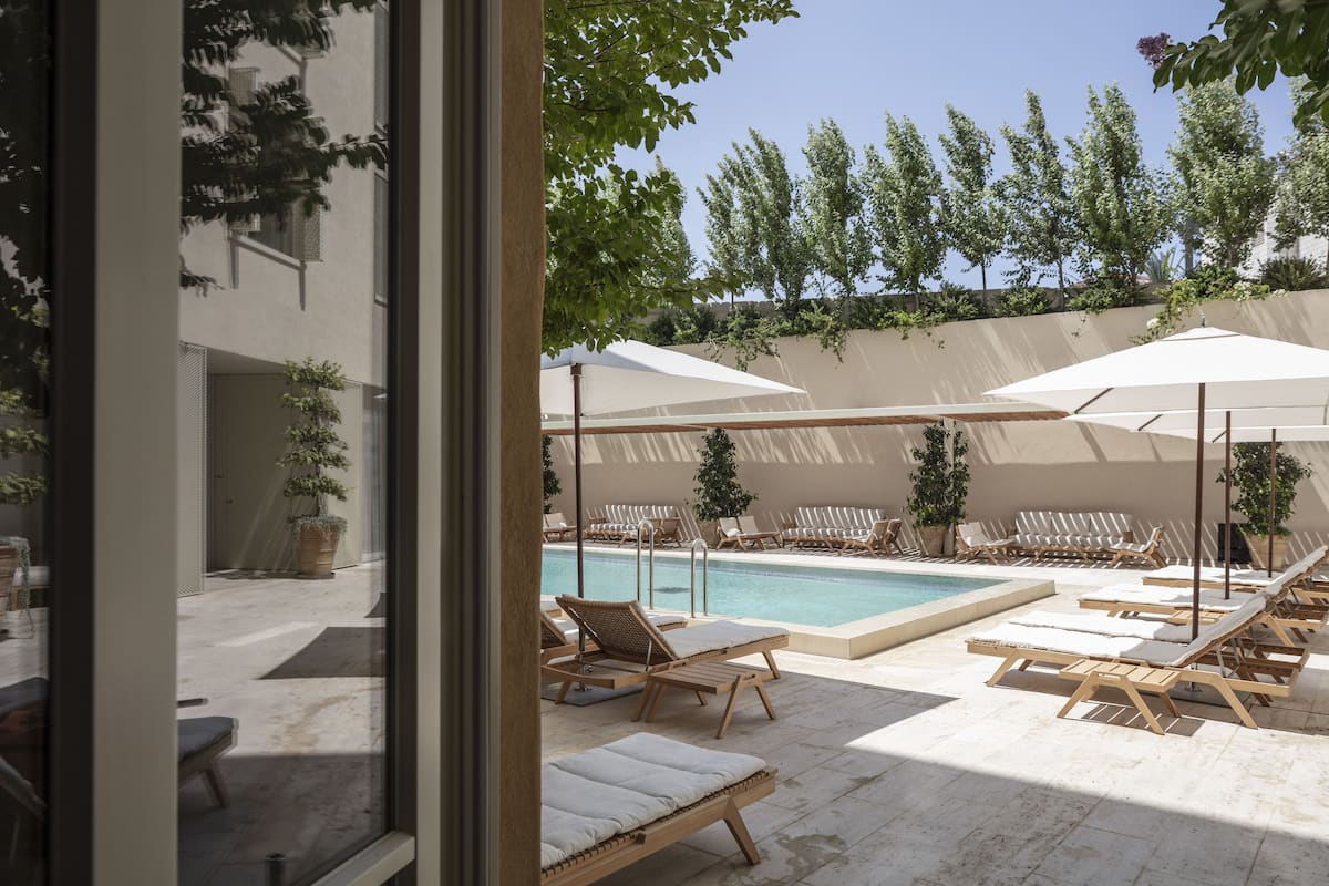 A poolside area with sun loungers and umbrellas, a clear sky, and a view of a building with a balcony.
