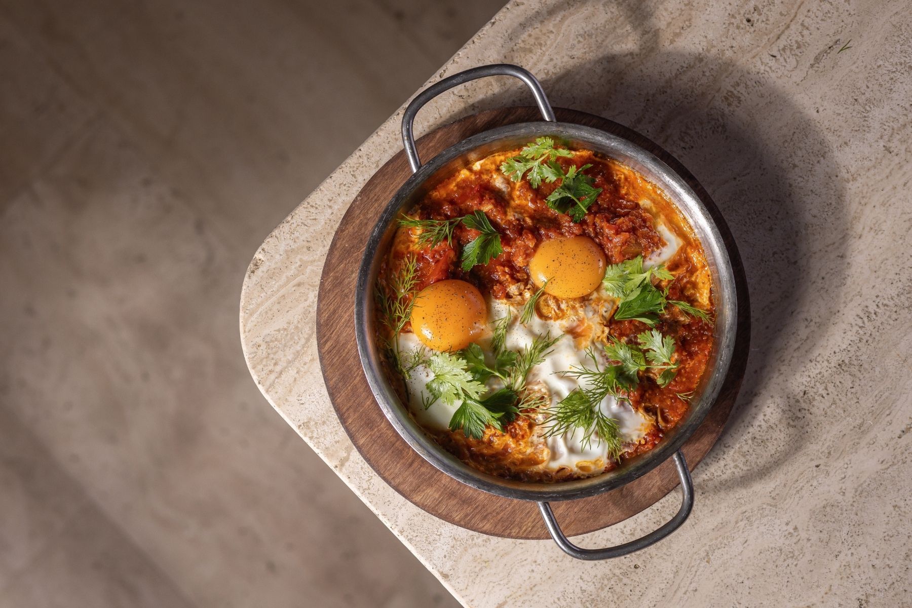 Un plato de shakshuka con huevos sobre una tabla de madera.