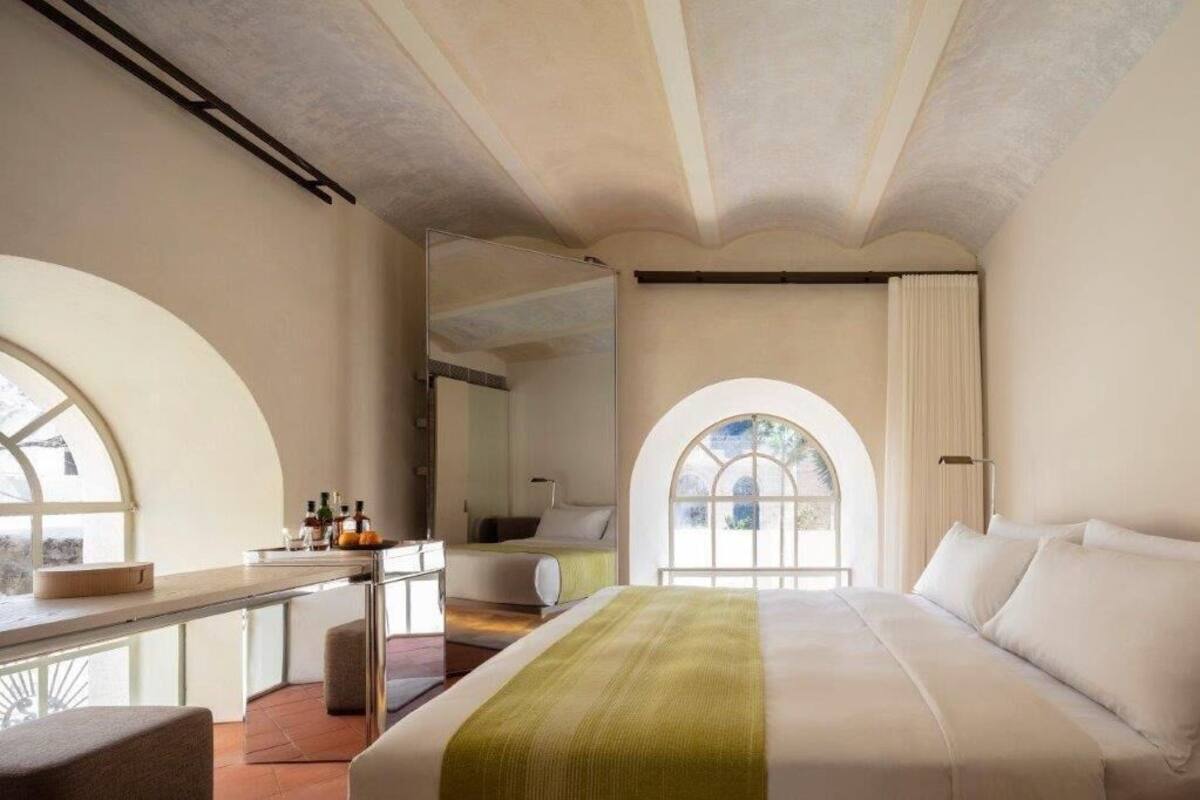 A hotel room with a large bed, a desk with toiletries, and arched windows.