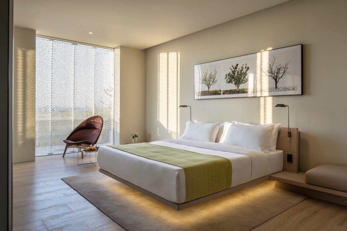 A modern bedroom with a large bed, a chair, and a painting on the wall.