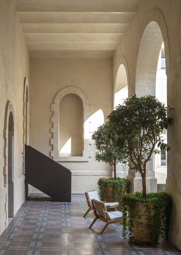 A covered outdoor area with a tiled floor, a staircase, and two wooden chairs. - The Jaffa – Fattal Limited Edition (Tel Aviv)
