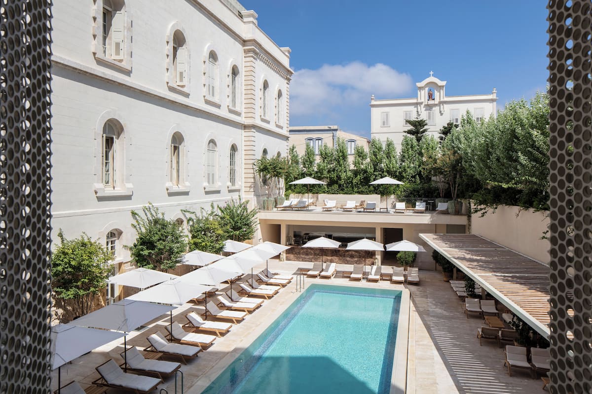 A pool area with lounge chairs and umbrellas, surrounded by buildings with arched windows and a bell tower.
