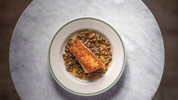 En tallrik med mat, med en bit panerad fisk ovanpå, serverad på en vit tallrik med en grön kant, placerad på ett marmorbord.
